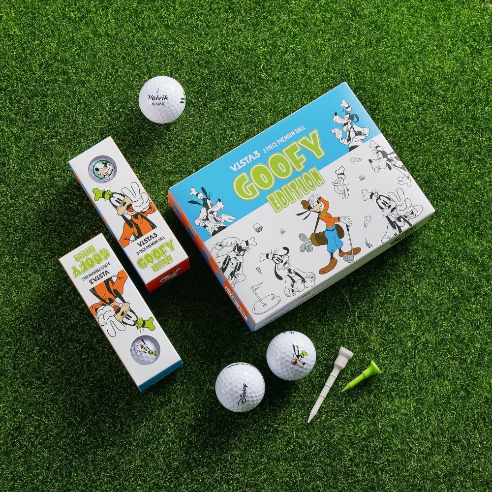 A set of golf balls with Goofy artwork on the packaging, along with golf tees and a box, displayed on a grass-like surface.