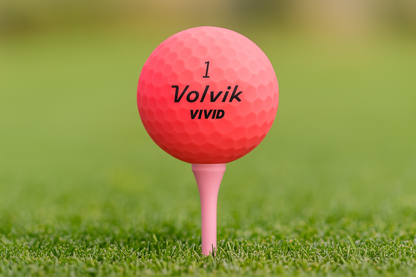 Pink golf ball with 'Volvik Vivid' branding on a tee in grass